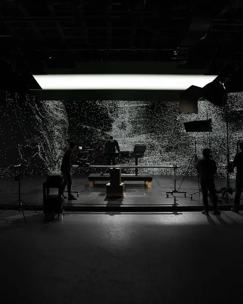 Dark studio with a huge light-speckled projection wall, crew in silhouette and an overhead softbox.
