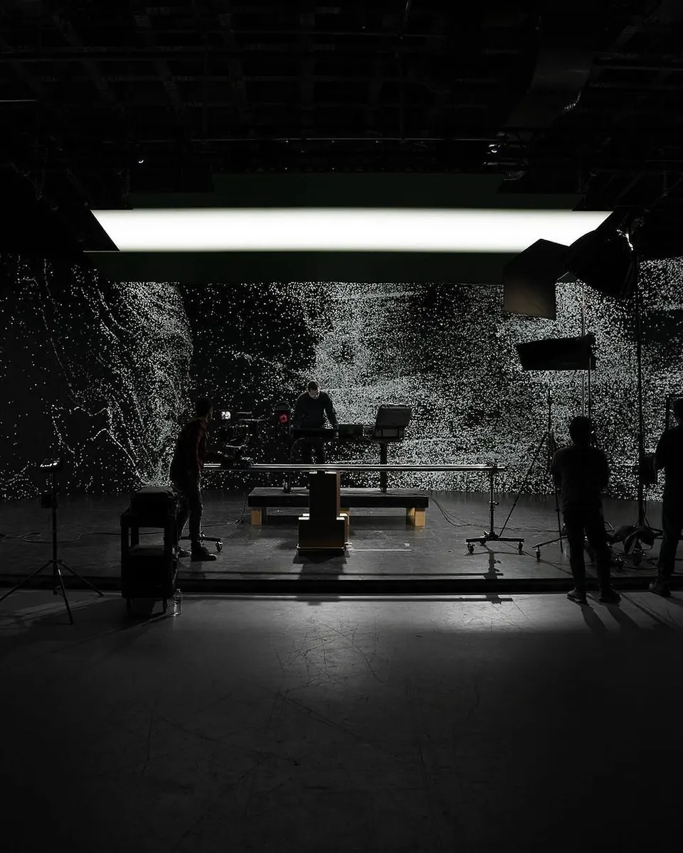 Dark studio with a huge light-speckled projection wall, crew in silhouette and an overhead softbox.