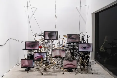Installation: a tangled drum kit with small screens showing eyes and mouths mounted among the stands.