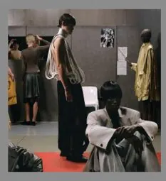 Fashion backstage scene: models in layered garments, one crouching on a red carpet.