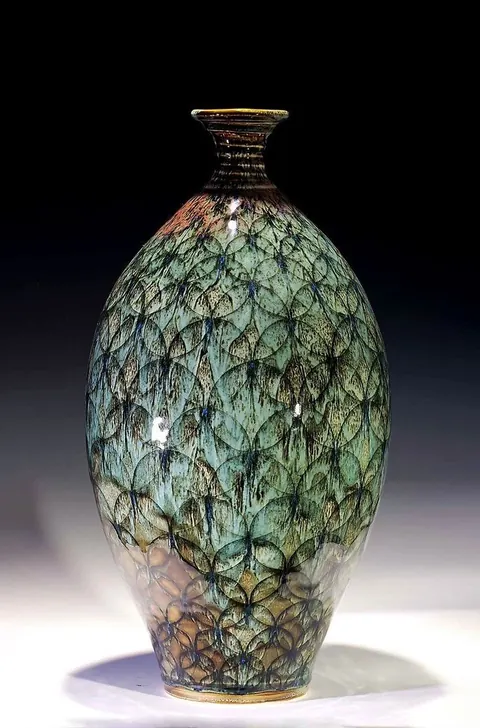 Ceramic vase with an intricate green and bronze leaf-pattern glaze against black.