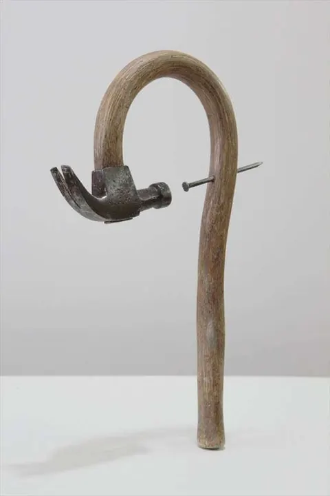 Conceptual sculpture: a hammer head nailed onto a bent wooden walking cane.