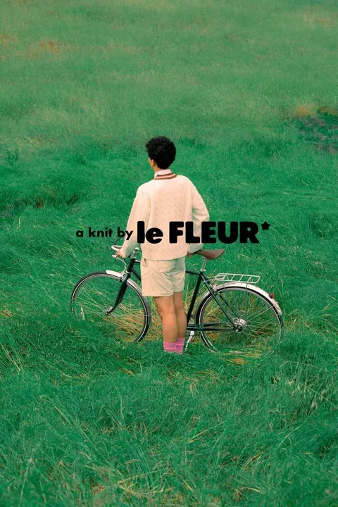 Fashion campaign image: a person in a cream knit sweater with a bicycle in tall grass, "a knit by le FLEUR*" wordmark.