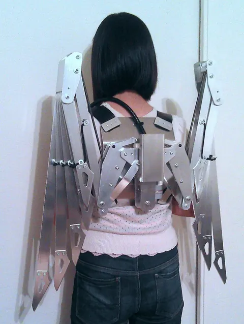 Person wearing a mechanical aluminium wing contraption strapped to their back.