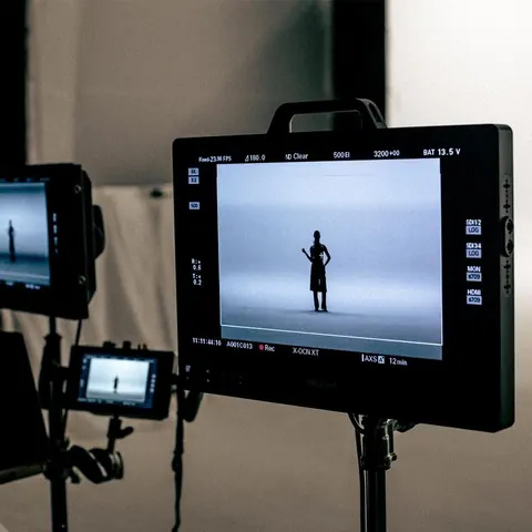 On-set field monitor showing a lone figure in a white studio, with a second monitor and rigging behind.