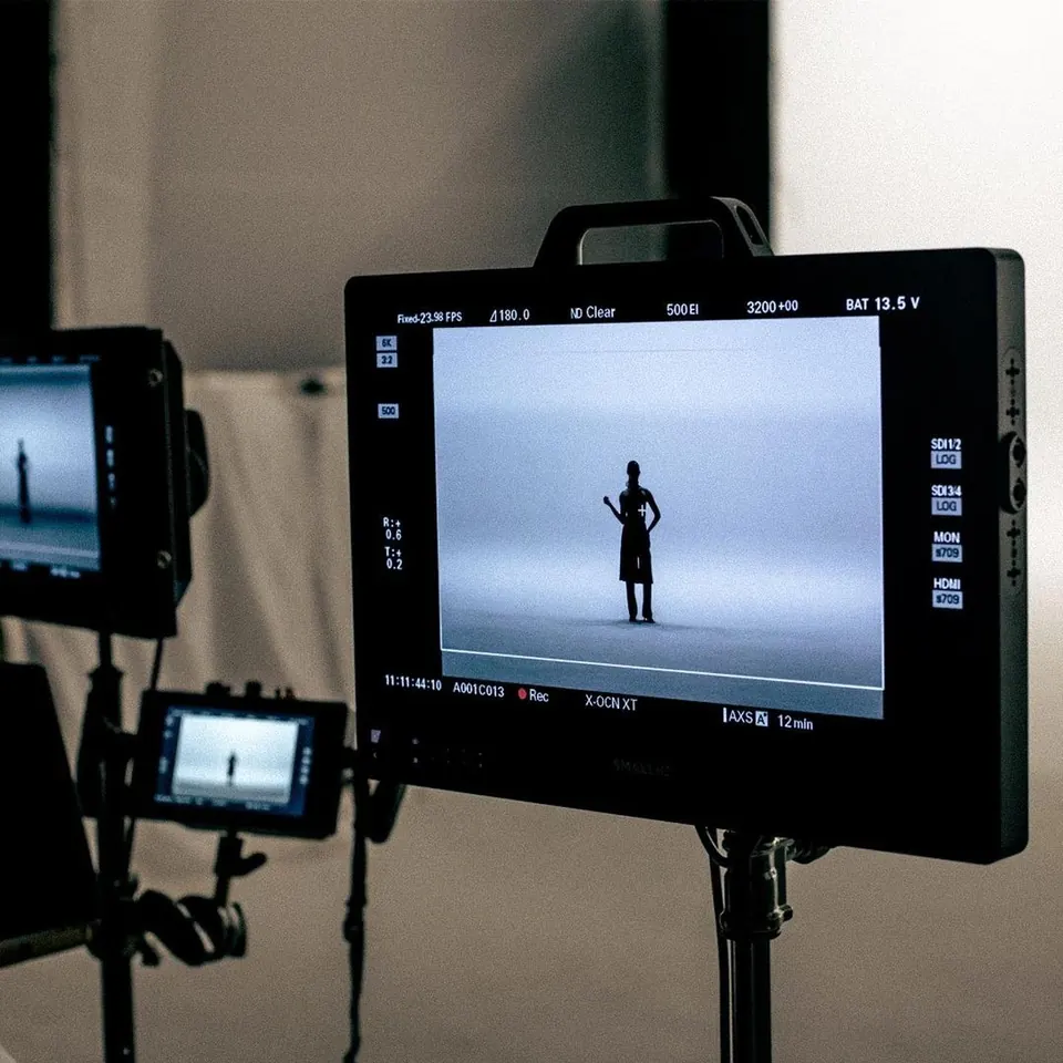 On-set field monitor showing a lone figure in a white studio, with a second monitor and rigging behind.