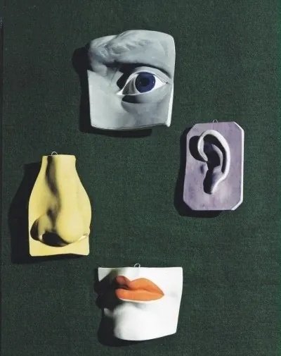 Plaster casts of an eye, ear, nose and lips, some painted yellow, lilac and orange, on dark green fabric.