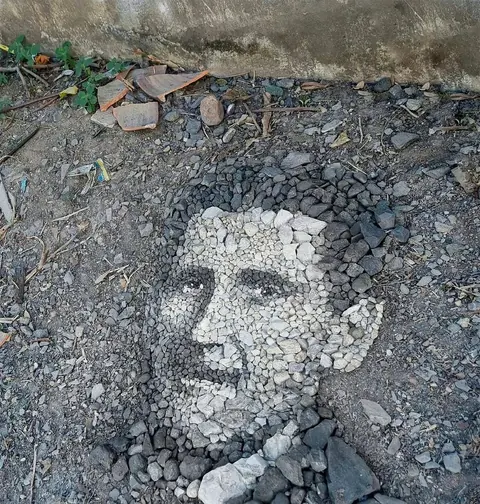 Portrait of a man's face made from light and dark pebbles arranged on the ground.