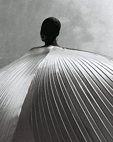 Black-and-white photo of a figure from behind wearing a huge pleated cape.