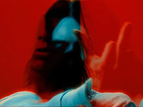 Experimental photo: motion-blurred woman with long hair in red and cyan light reaching toward the camera.