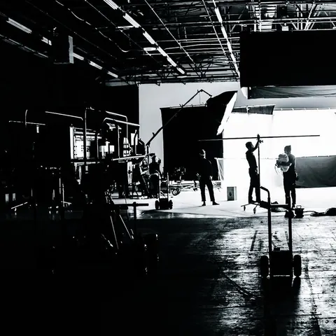 Black-and-white photo of a large soundstage: crew silhouettes against a bright white backdrop, lighting rigs overhead.