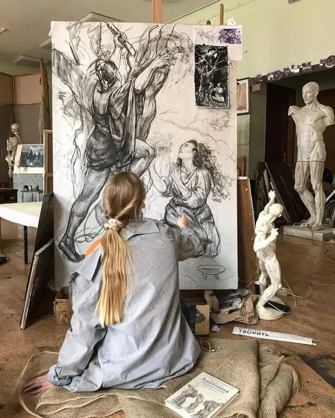 Art student with a long ponytail drawing a large charcoal figure composition in a studio full of plaster casts.