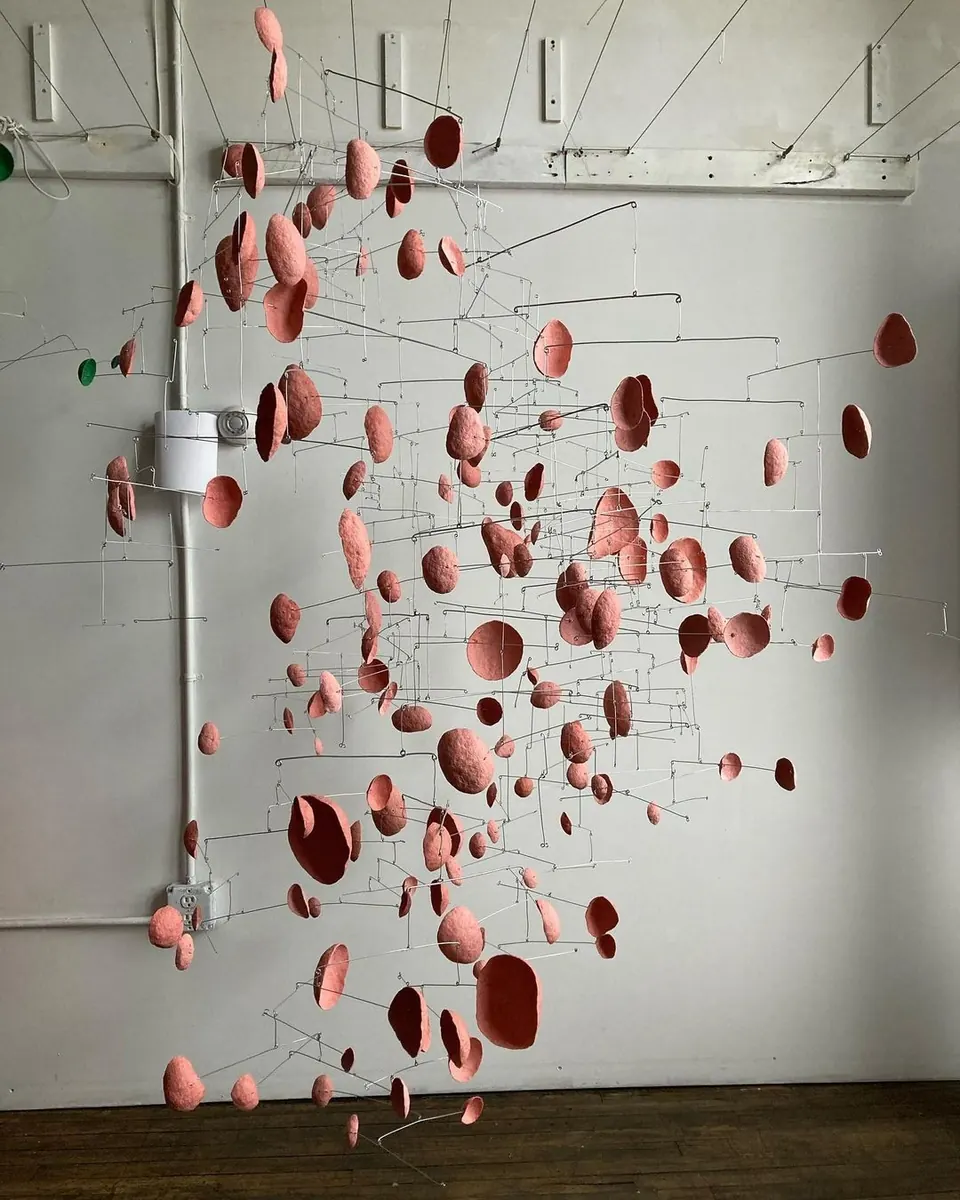 Installation of hundreds of coral-pink discs suspended on thin wires in a white studio.
