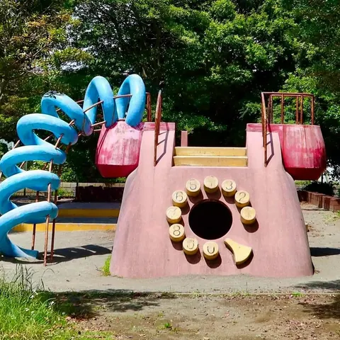Photograph of a quirky playground: a pink rotary-telephone-shaped climbing structure with blue spiral slides.