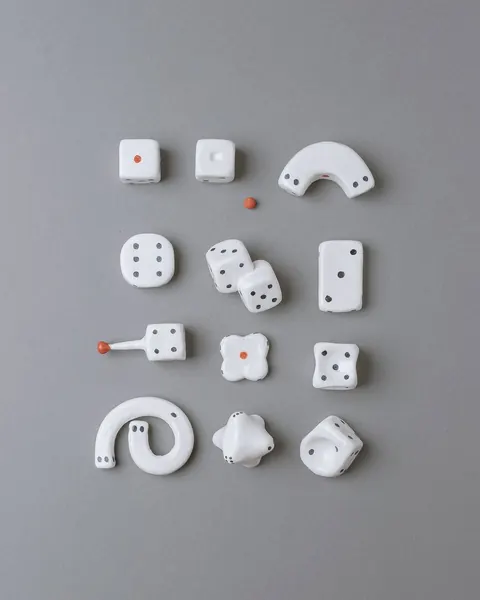 Playful white ceramic objects shaped like dice, hooks and knobs with red dots, on grey.